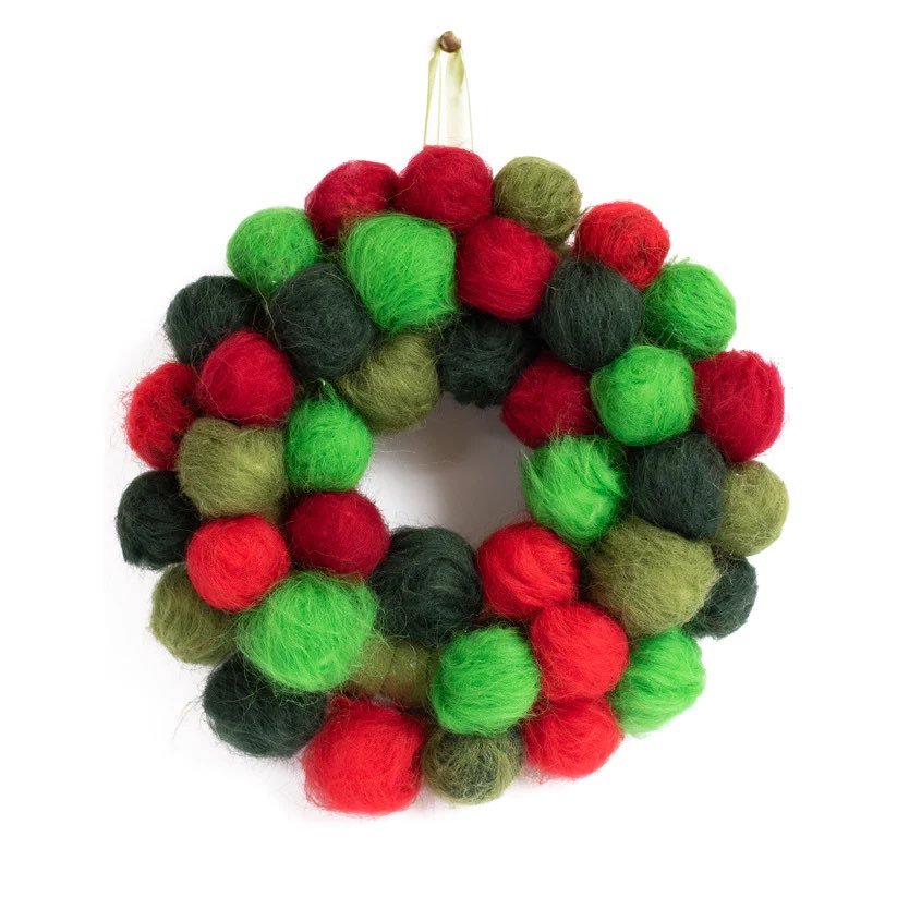 a completed christmas pom pom wreath hanging on a ribbon, featuring various shades of green, red, and yellow