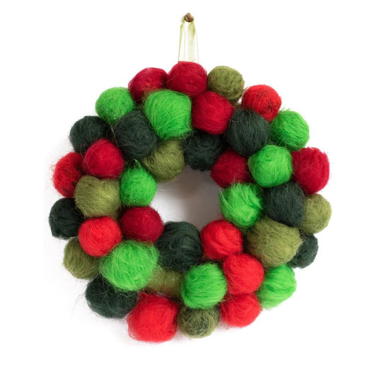 a completed christmas pom pom wreath hanging on a ribbon, featuring various shades of green, red, and yellow