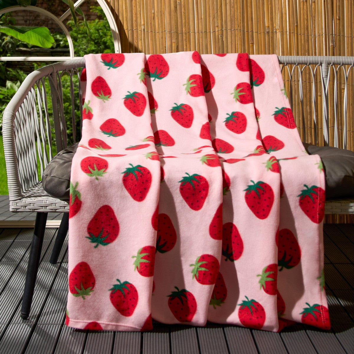 strawberry fleece throw draped over garden bench showing playful strawberry pattern design